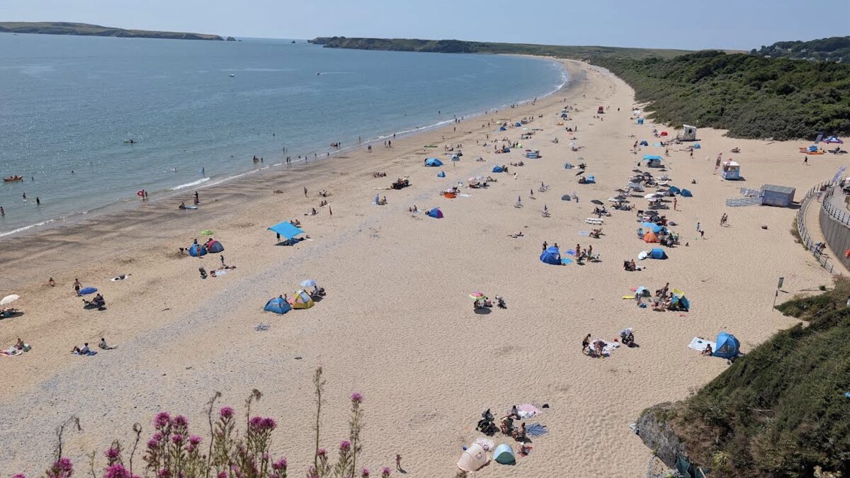 Tenby South Beach in high summer, families and tents spread along the long sand with Caldey Island across the water