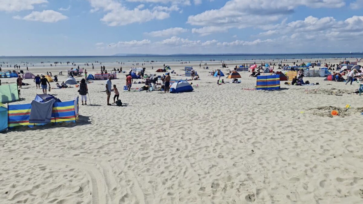 West Wittering's wide flat sand in August, windbreaks and family camps spread toward the distant sea