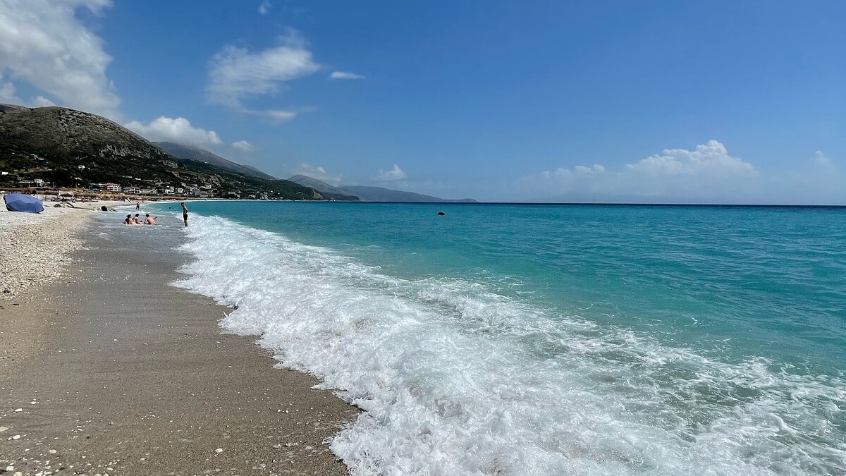 The long, near-empty sand and shingle sweep of Borsh beach on the Albanian Riviera, backed by olive groves and mountains