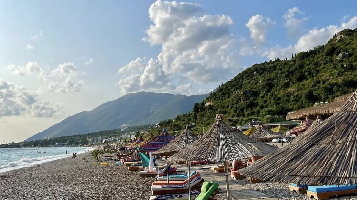 The long pebble beach at Dhermi on the Albanian Riviera, rows of beach-club umbrellas and sunbeds along the shore