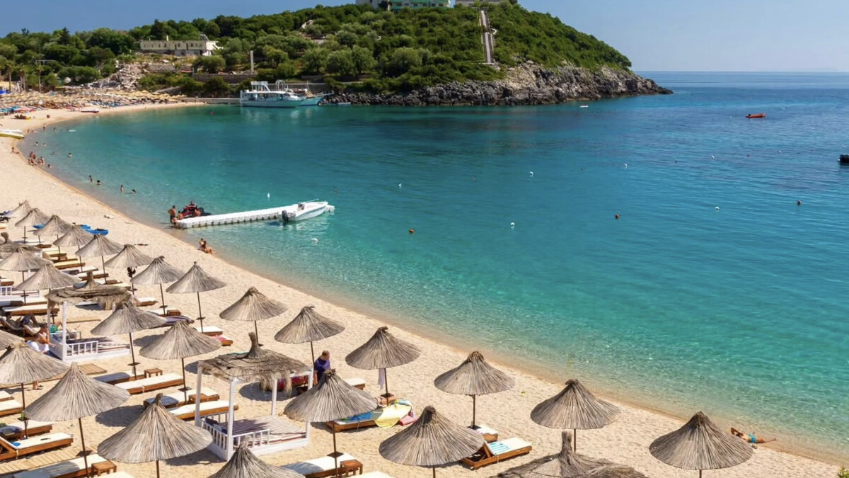 The compact turquoise bay of Jale on the Albanian Riviera, a beach-club row of thatched umbrellas along the shore