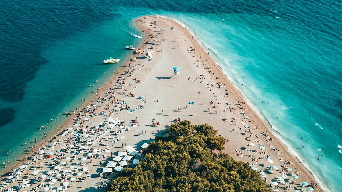 Aerial view of Zlatni Rat at Bol on Brac island, the white pebble spit extending into deep blue water with boats moored along its edges