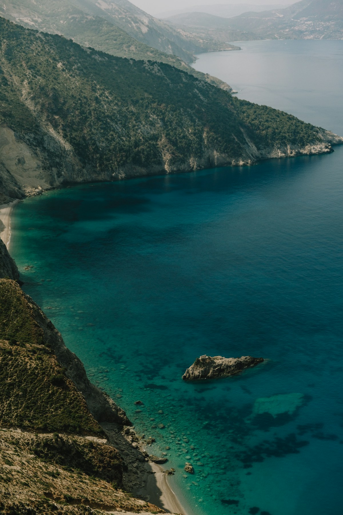 Dramatic white pebble beach with turquoise water and tall green cliffs at Myrtos, Kefalonia