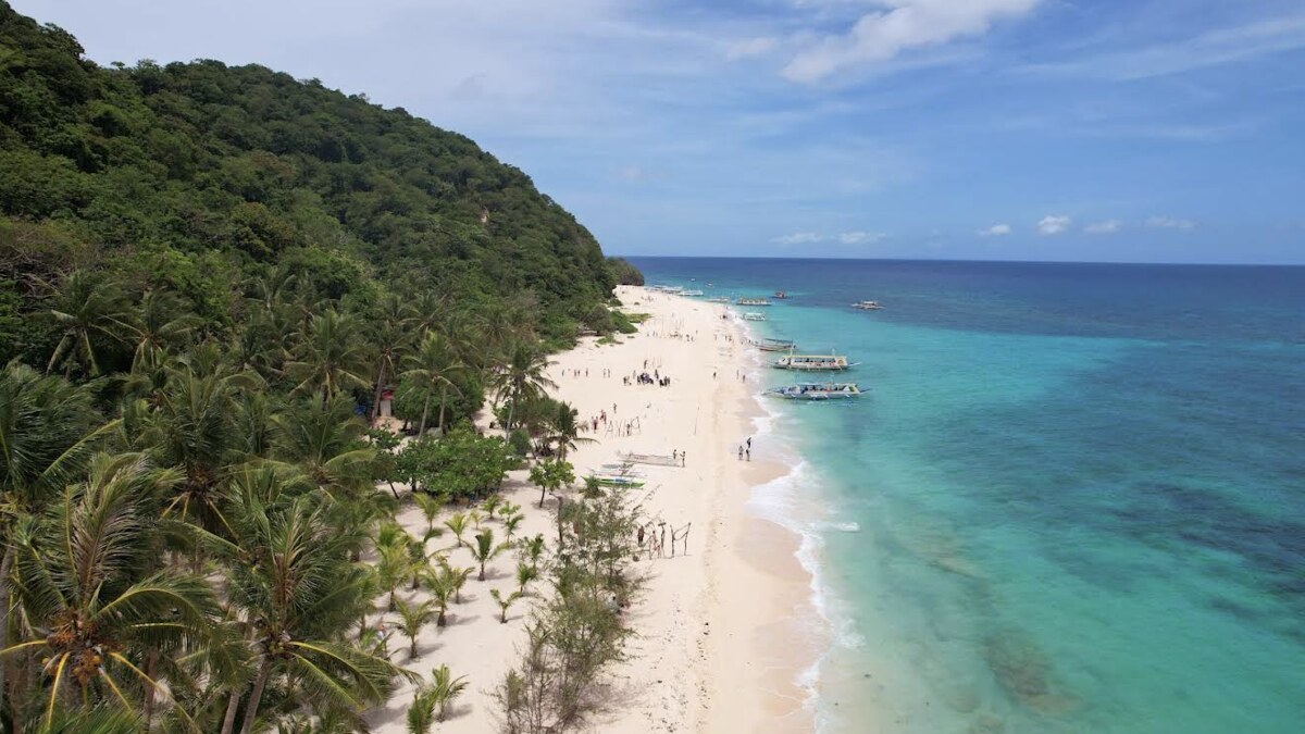 Aerial of Puka Beach on Boracay, a long white-sand beach along a forested coast with calm turquoise water and few people