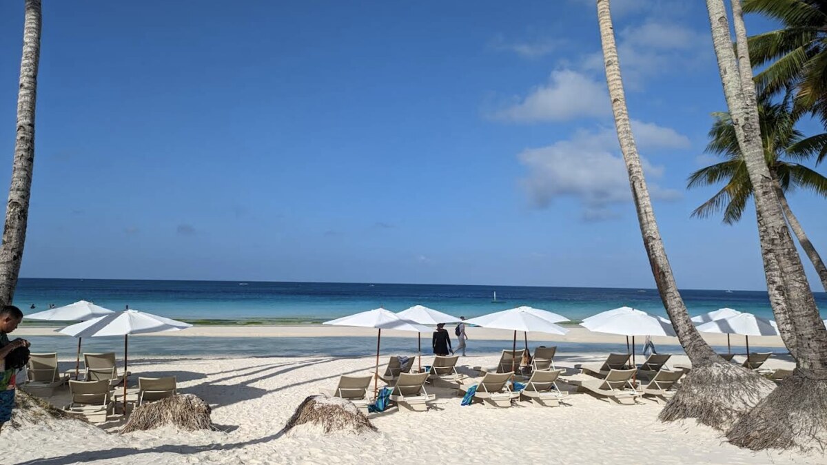 Rows of sun loungers and umbrellas on the powder-white sand of White Beach, Boracay, beneath palms beside the turquoise water