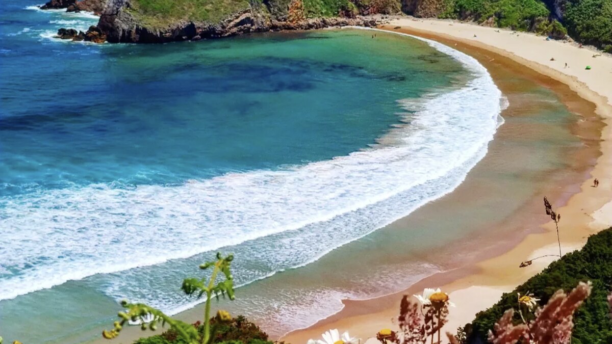 Playa de Torimbia near Llanes from the trail above, a half-moon of golden sand and turquoise water enclosed by green cliffs