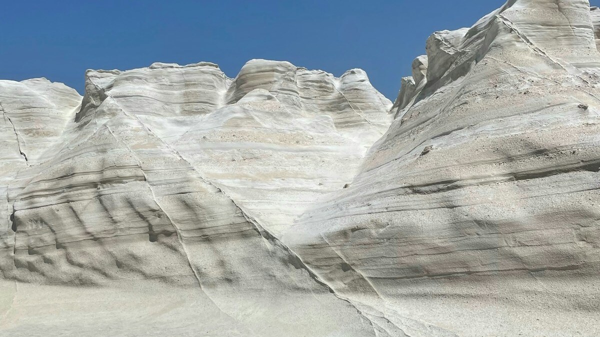 The white volcanic rock formations of Sarakiniko on Milos, smooth wind-carved moonscape ridges under a deep blue sky