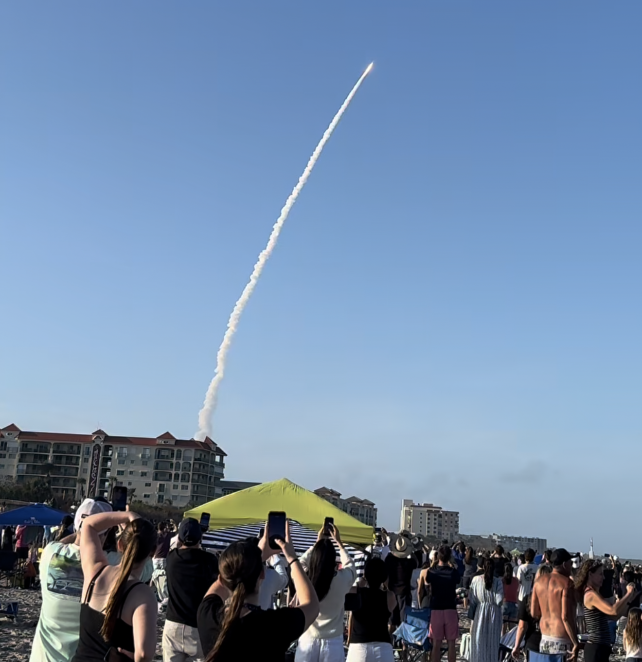 Crowd on Cocoa Beach watching a rocket launch trail rising into the sky from Cape Canaveral
